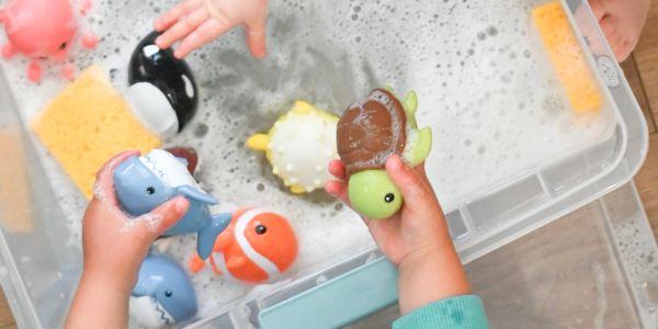 Children playing with animal bath toys and sponges in a tub.
