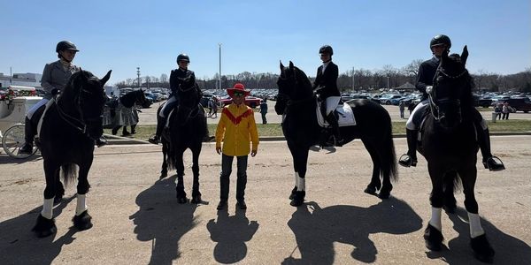 Four riders on black horses with a person in a yellow and red jacket standing between them.