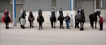 Seven people with horses standing in a row indoors.