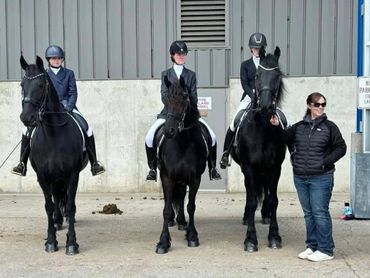 Three riders on black horses with a handler standing beside them.