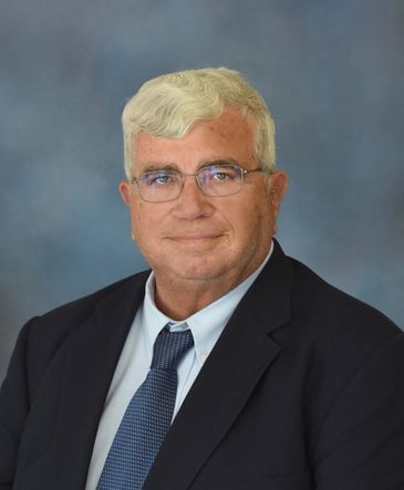 Professional portrait of an older man in a suit and tie with glasses.