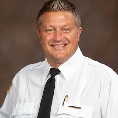 Smiling man in white uniform with black tie.