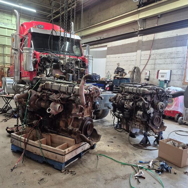 Two large engines in a repair shop with a red truck cab.