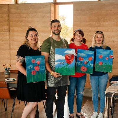 Four people proudly display their flower paintings after a fun art session.