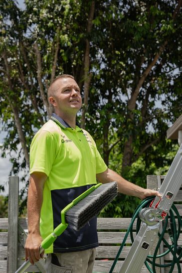 Worker in a bright uniform holding a brush and standing by a ladder outdoors.