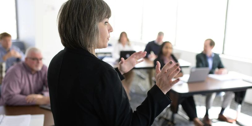 Woman presenting to a group in a meeting room.
