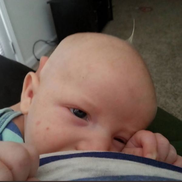 Close-up of a baby resting and sucking on someone's shirt.