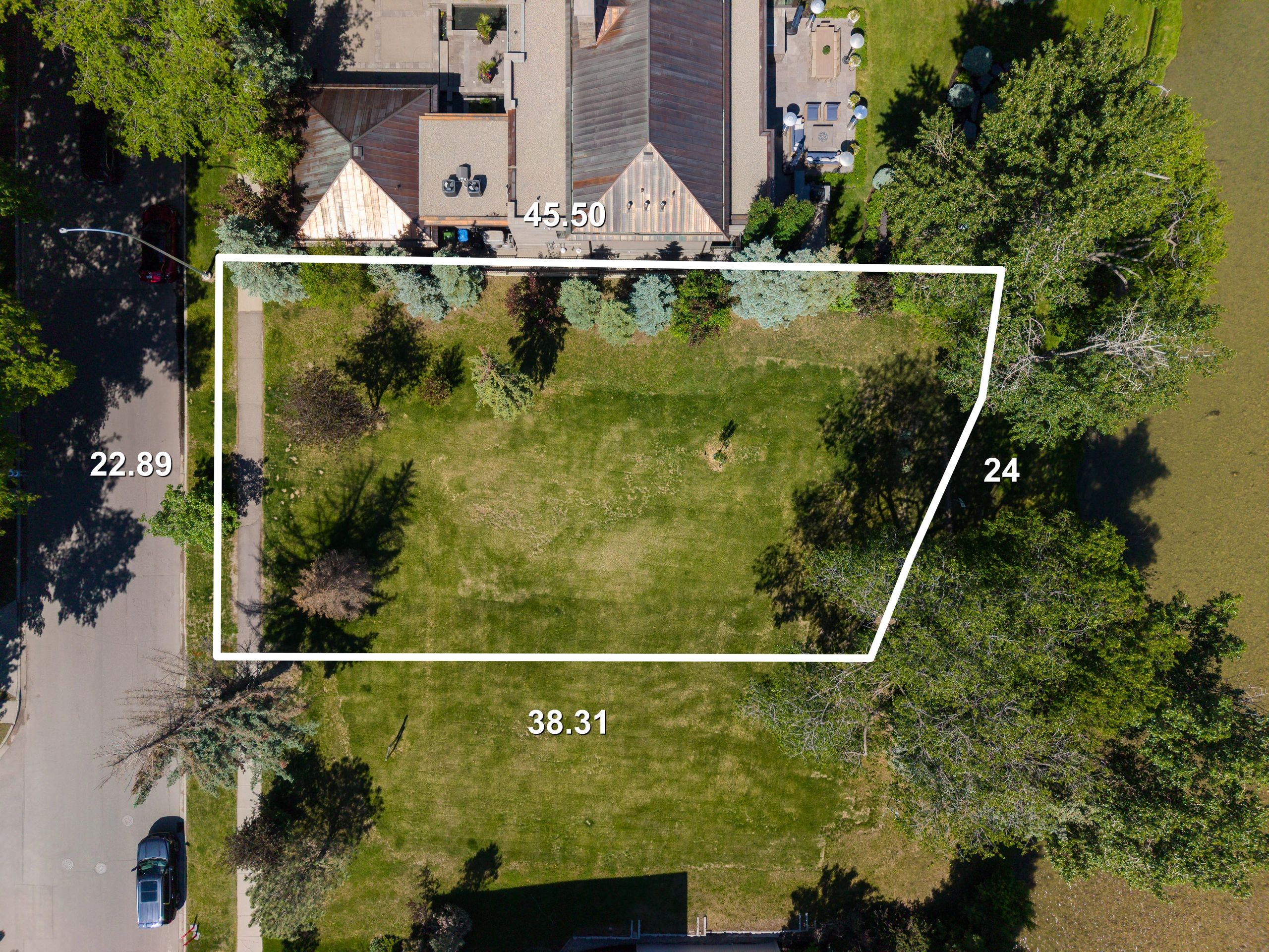 Aerial view of a green lot outlined with white lines showing dimensions near buildings and trees.