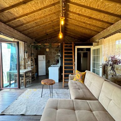Cozy rustic living space with wooden ceiling, beige sofa, and small kitchen.
