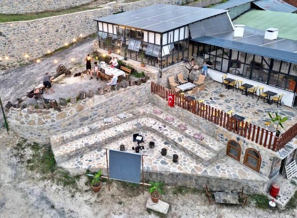 Outdoor stone terrace with seating and fire pit near a glass-walled building.