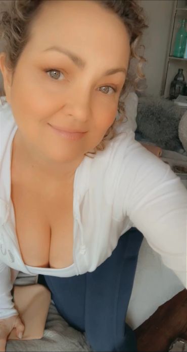 Smiling woman with curly hair taking a close-up selfie.