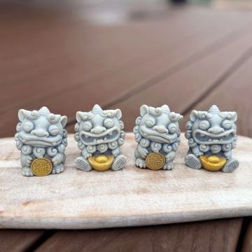 Two small gray statues of Chinese guardian lions or 'Foo Dogs.' One holds a golden ingot, and the ot
