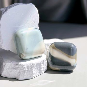 Two handcrafted, pebble-shaped soaps with marbled stone patterns in soft earth tones.