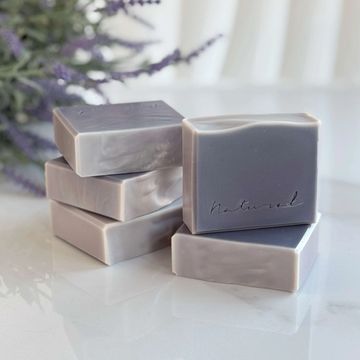 Stack of handcrafted lavender-colored natural soaps, one bar stamped with the word “natural.”