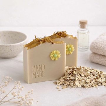 Handmade oatmeal soap decorated with yellow flowers and herbs, styled with natural elements.