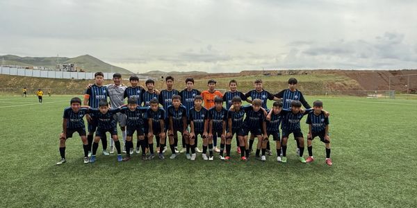Youth soccer team posing together on a green field under a cloudy sky.