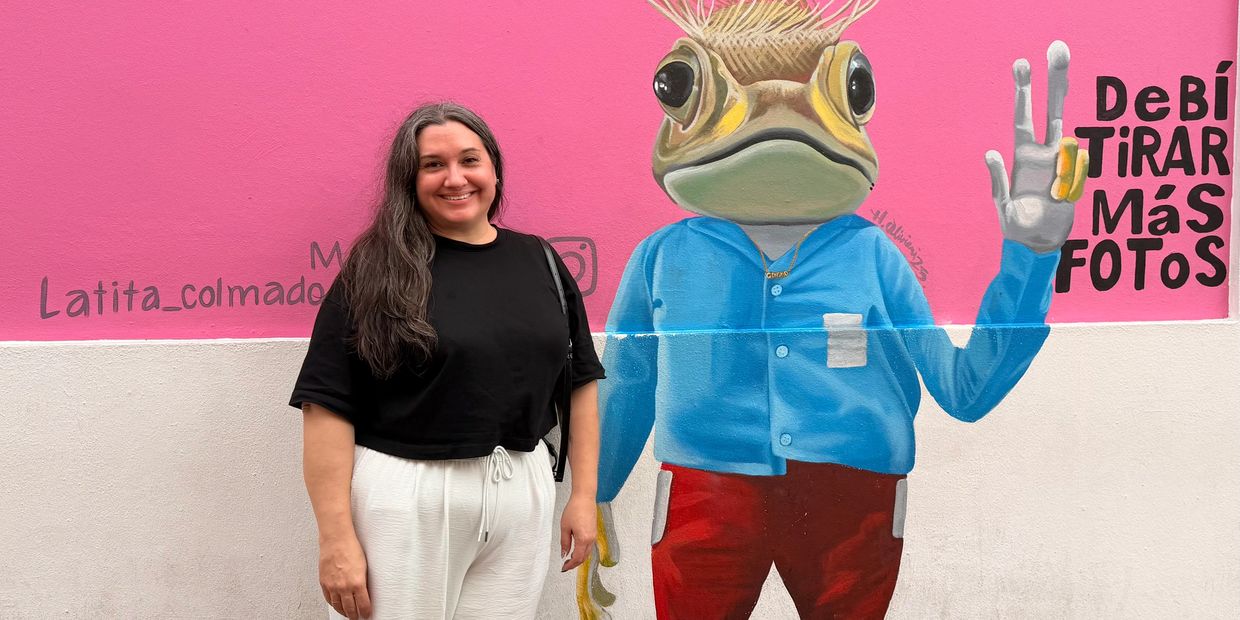 Woman posing next to colorful frog mural.
