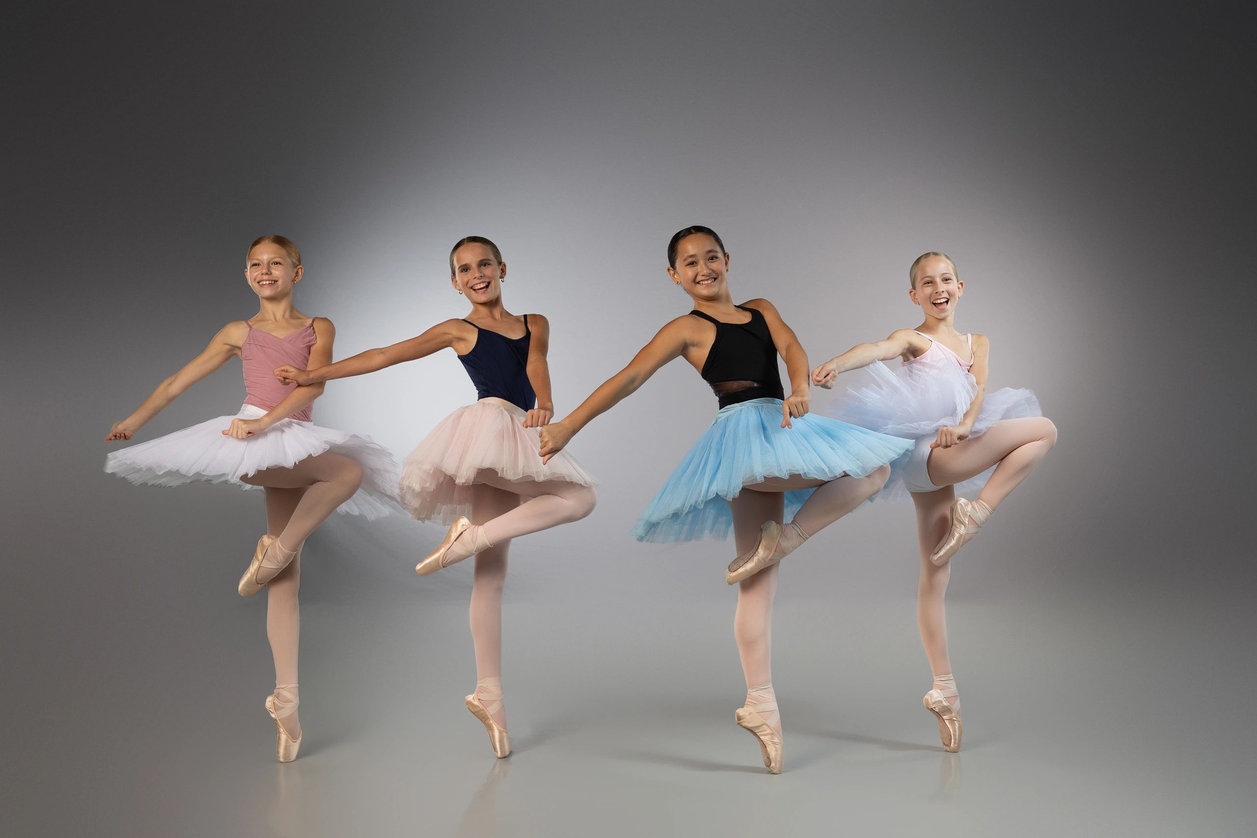 Four young ballerinas in colorful tutus dancing gracefully in a studio.