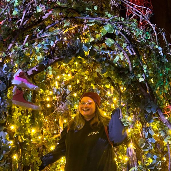 Person smiling under an arch of greenery and lights.