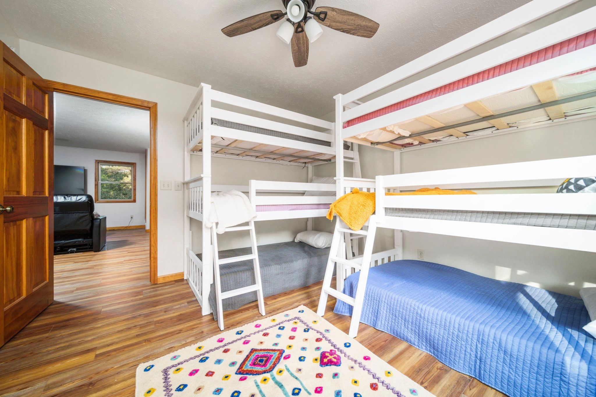 A room with bunk beds, a ceiling fan, and a colorful rug.
