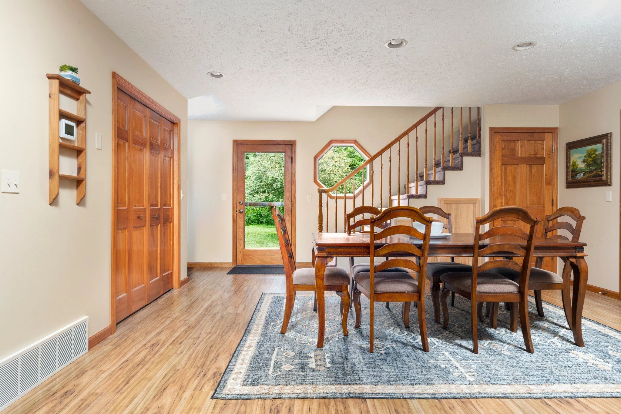 A dining area with a wooden table and chairs, a staircase, and a door leading outside.