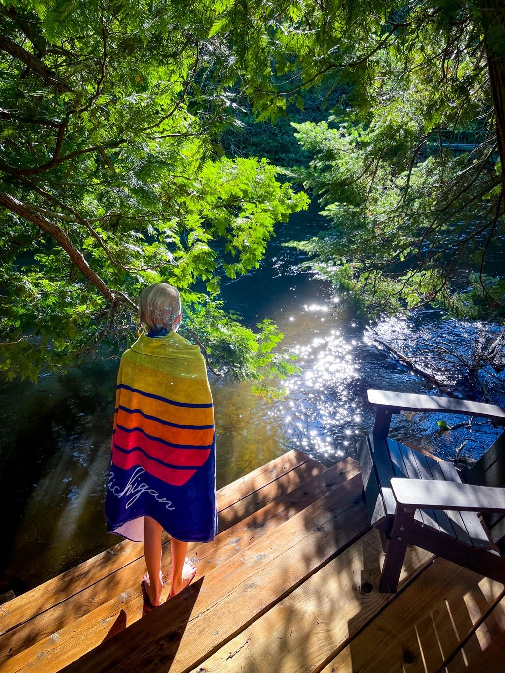 A child stands on a wooden deck overlooking a river.