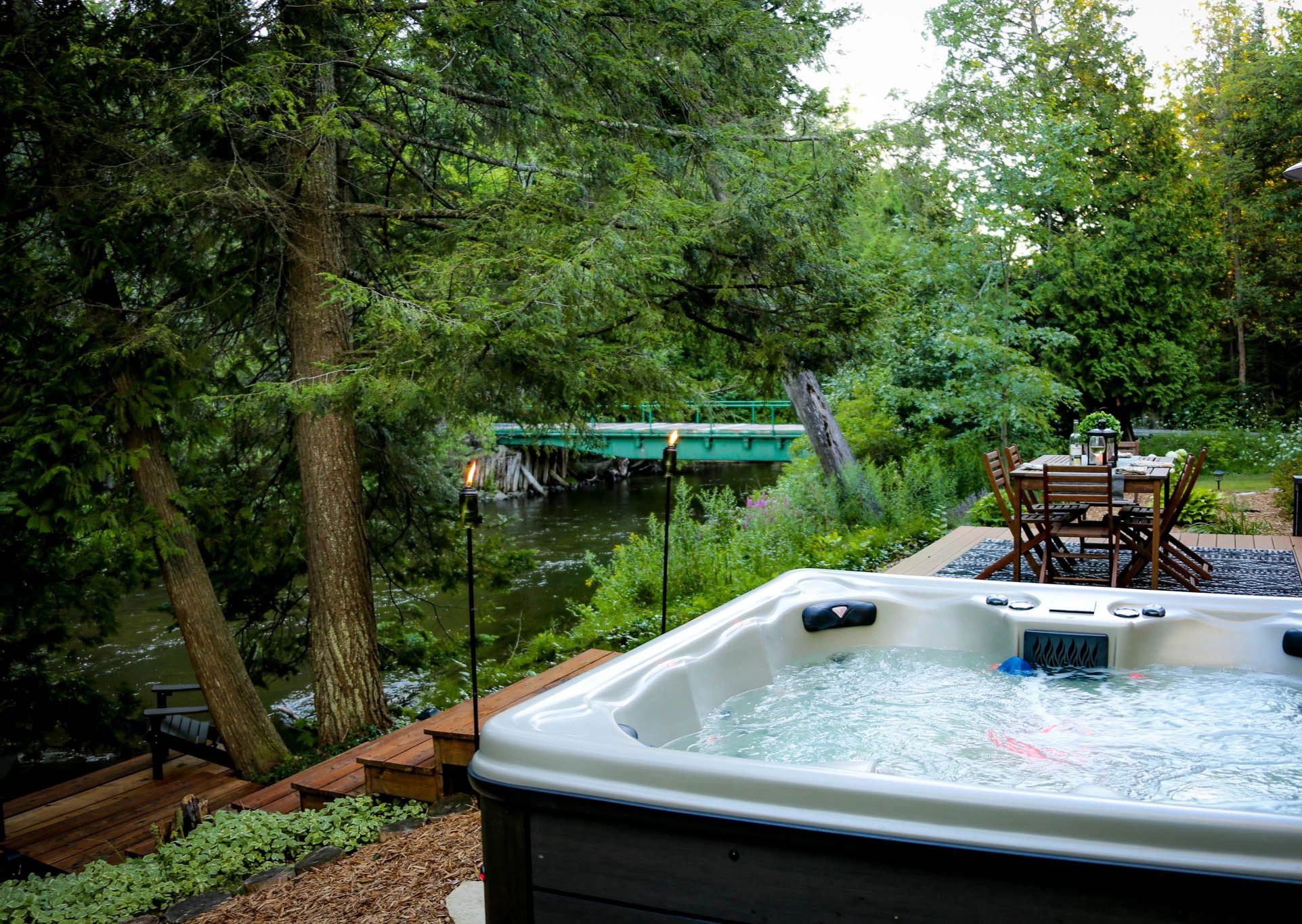 A hot tub on a deck overlooking a river with trees and a bridge in the background.
