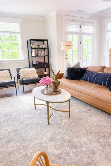 Bright living room with tan sofa, black chairs, and a round marble coffee table.