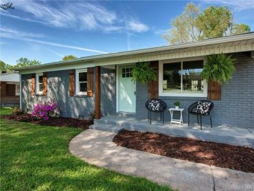 Cozy gray brick house with wooden shutters and a small porch seating area.