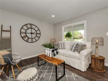 Cozy living room with white sofa, rustic wooden table, and decorative wall clock.