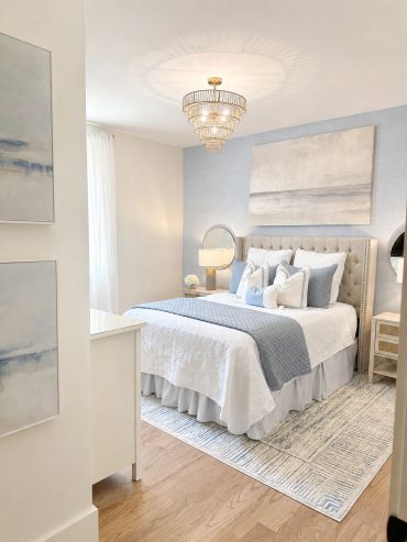 Bright bedroom with soft blue and white decor, elegant chandelier, and cozy bedding.