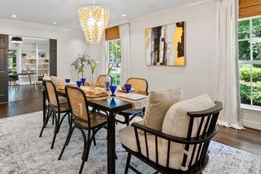Dark hardwood floors and white walls in a dining room with two windows with blinds and curtains.