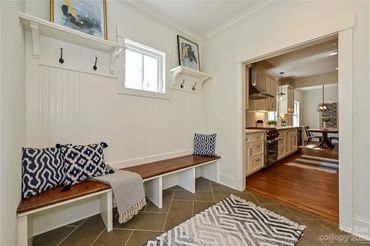 Mudroom with a built-in bench, hooks, shelves, a patterned rug, and a view into a kitchen.