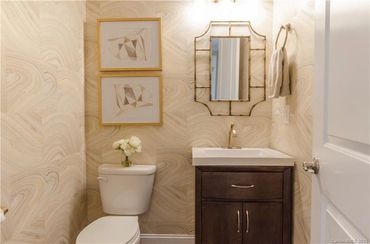 Powder room with patterned wallpaper, a dark wood vanity, a rectangular mirror, and framed artwork.