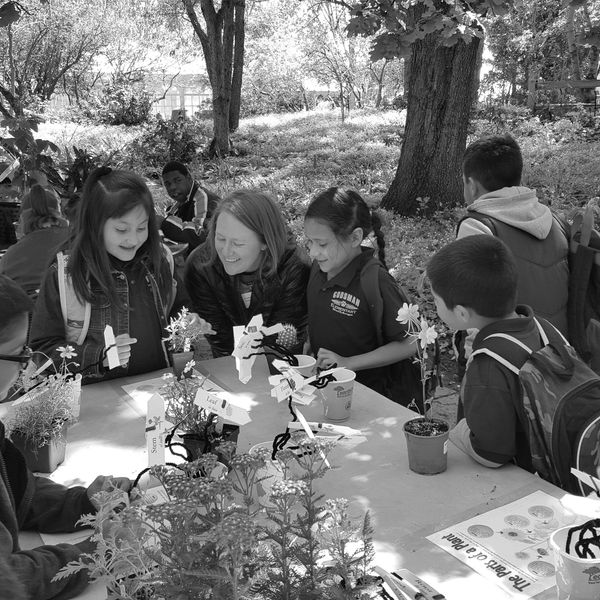 Heather Dorrell surrounded by five students and pointing to a flower bloom.