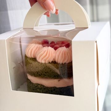 A mini cake with pink frosting inside a white cake box with a handle.