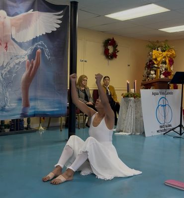 A woman in white dance attire performing a seated dance in a church setting.
