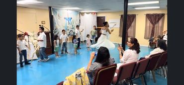 Children performing a dance in a small indoor venue with an audience.
