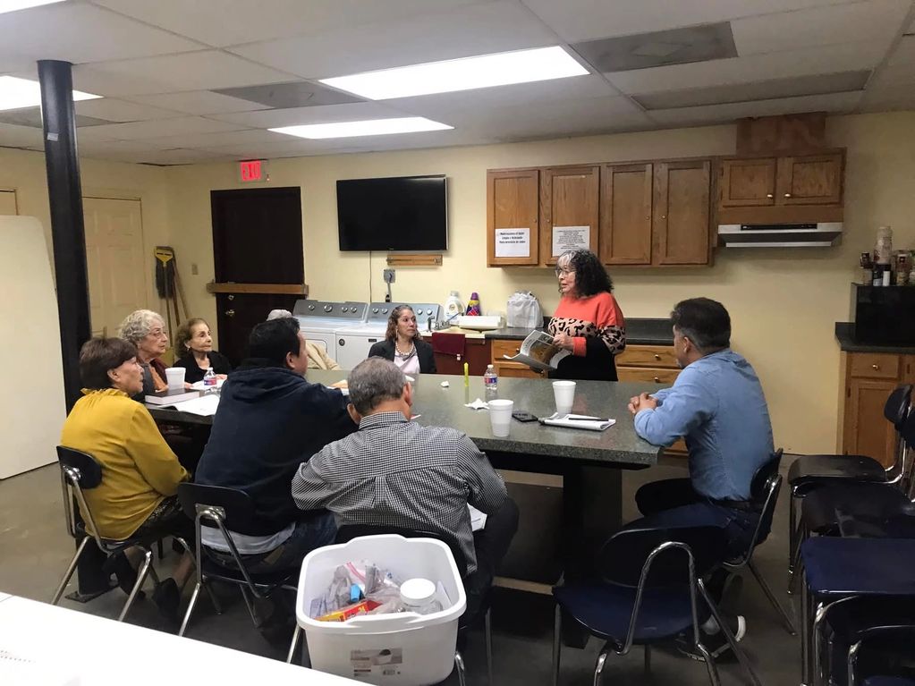 A group of people attending a meeting in a kitchen-like room.