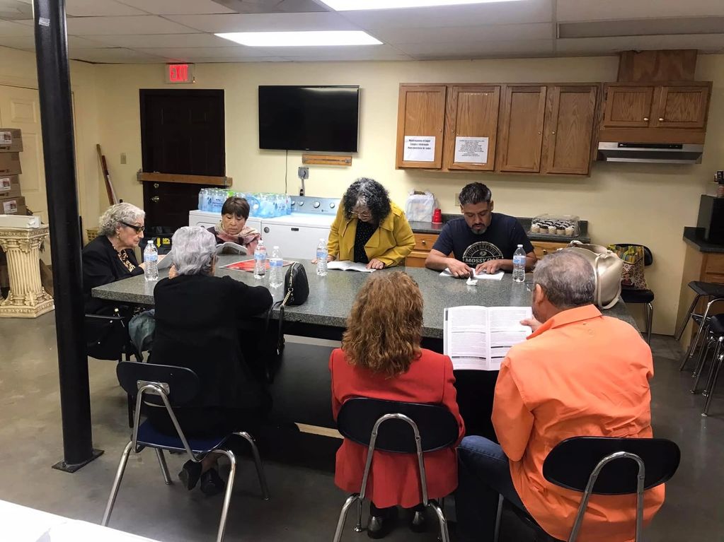 A group of adults engaged in reading or studying around a table in a casual room.