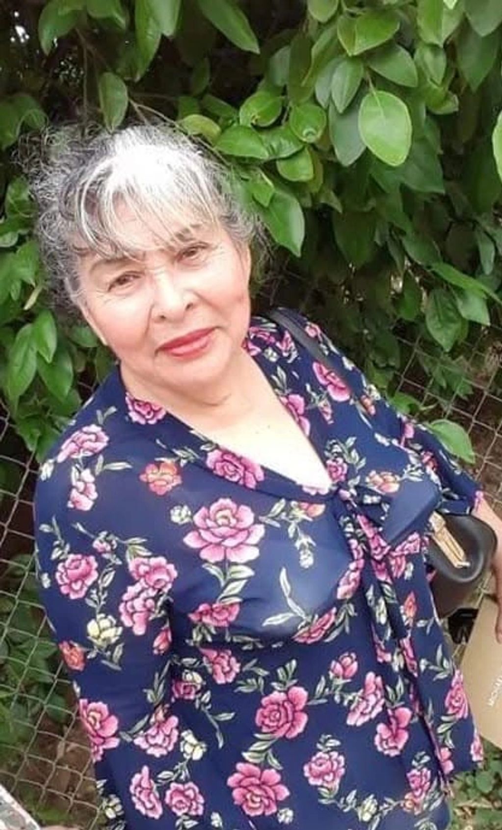 Smiling elderly woman in a floral dress standing outdoors.