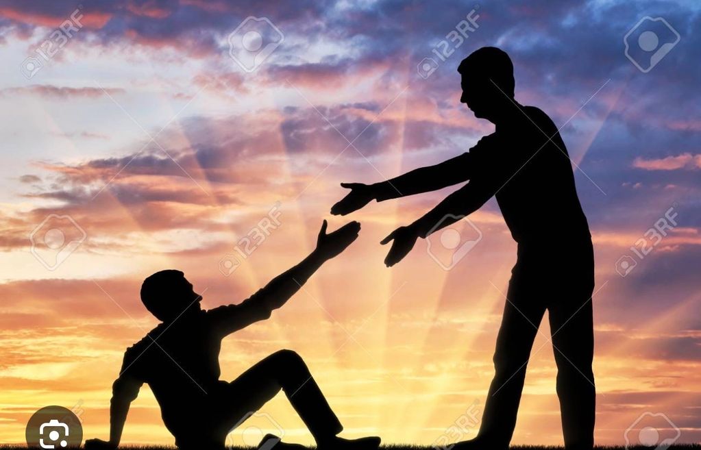 Silhouettes of two people reaching out to help each other at sunset.