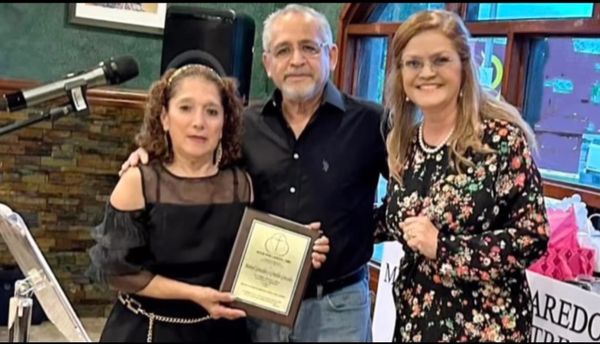 Three people posing with an award plaque indoors.