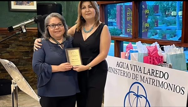 Two women smiling, holding a plaque at a marriage ministry event.