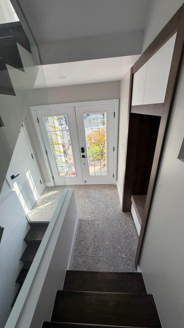 Entrée moderne avec escalier et porte vitrée.