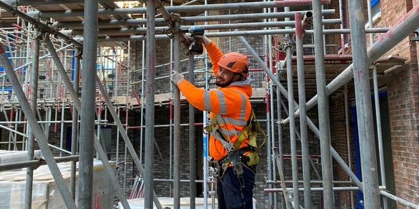 Construction worker in orange safety gear working on scaffolding.