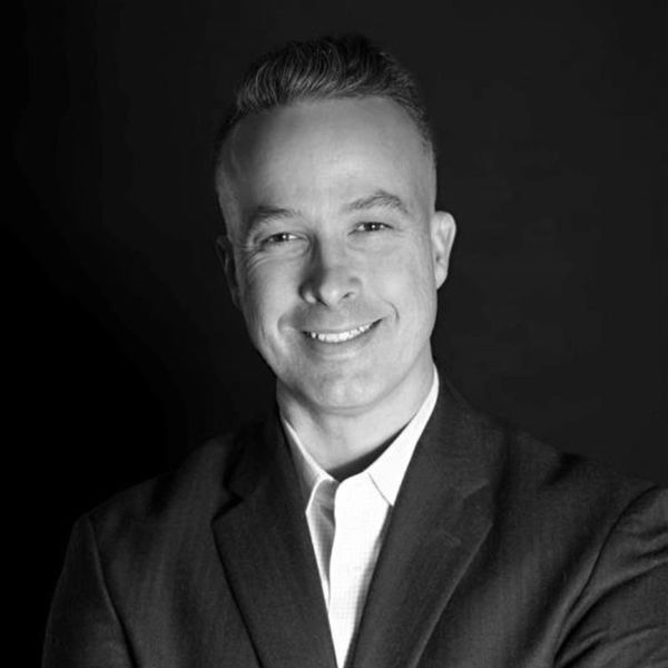 Black and white portrait of a smiling man in a suit against a dark background.