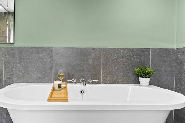Modern bathtub with candle, wine glass, and plant.