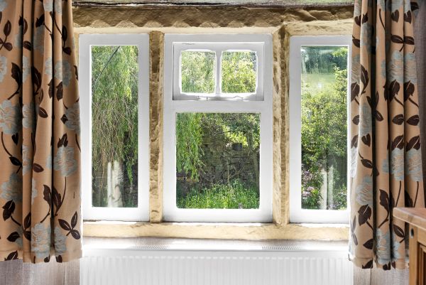 Window view of green garden through cream-colored curtains.