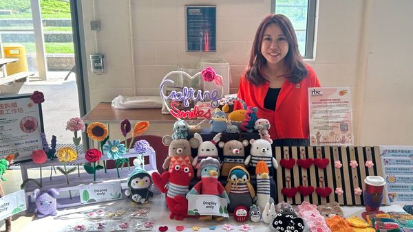 Woman smiles behind a table of colorful crocheted toys and flowers.